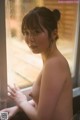 A naked asian woman looking out of a window.