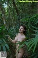 A naked woman standing in the middle of a forest.