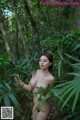 A naked woman standing in the middle of a forest.