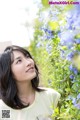 A woman standing in front of a bush of blue flowers.