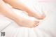 A woman's bare feet on a bed with white sheets.