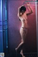 A naked woman standing in a shower next to a glass door.