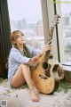 A woman sitting on the floor with a guitar.