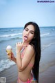 A woman in a bikini eating an ice cream cone on the beach.