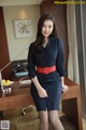 A woman in a blue dress standing next to a desk.