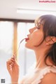 A woman in a white dress holding a spoon in her mouth.