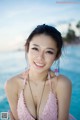 A woman in a pink bikini posing by the water.