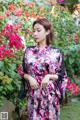 A woman standing in front of a bush of flowers.