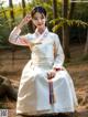 A woman in a white hanbok sitting on a tree trunk.