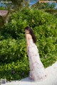 A woman in a white dress standing in front of a bush.